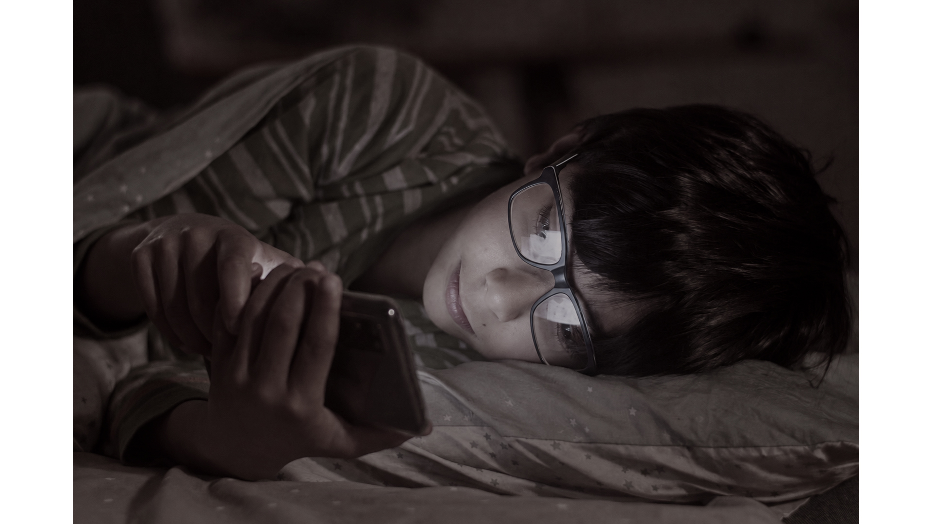 Menino de óculos usando um celular enquanto está deitado